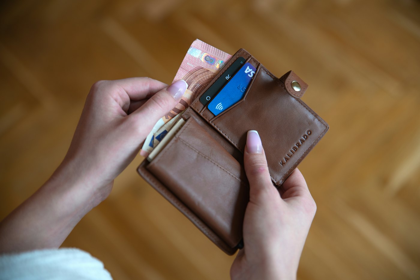 A hand holding a slim brown leather card wallet