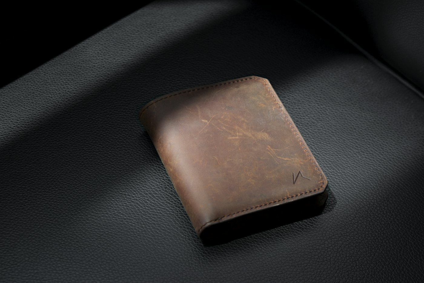 A brown leather bifold wallet laid on dark leather